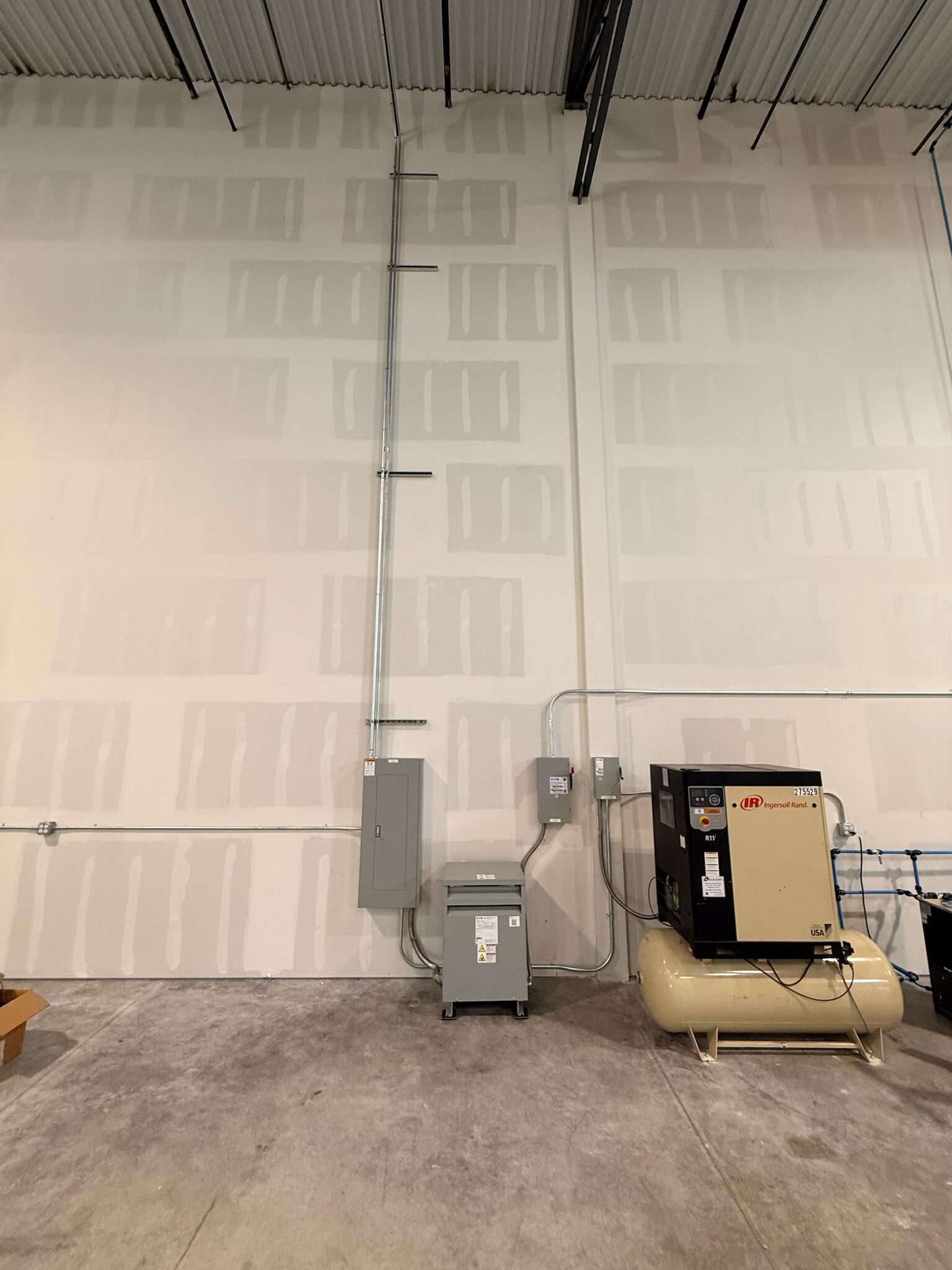 Wide shot of transformer, distribution panel, and Ingersoll Rand compressor in commercial warehouse — Cyber Electric LLC