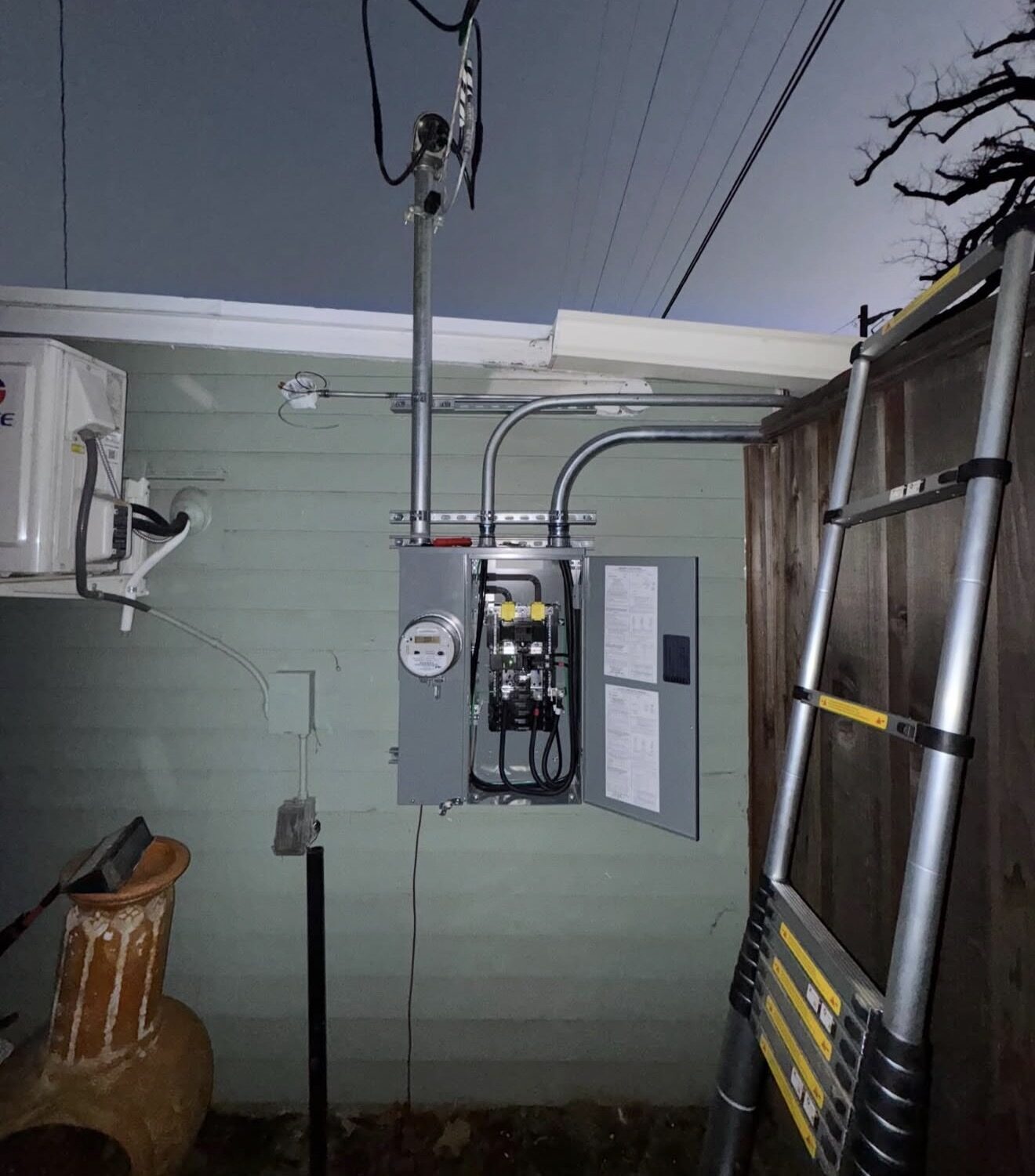 New 200A service entry at night — conduit sweeps up exterior wall to weatherhead, panel door open — Cyber Electric LLC, Modesto CA