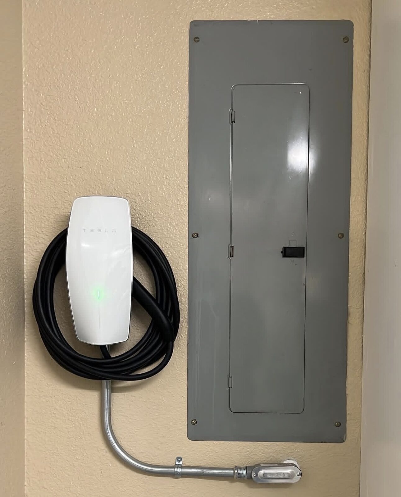 Tesla Wall Connector installed on stucco garage wall next to electrical panel with conduit run — Cyber Electric LLC, Modesto CA